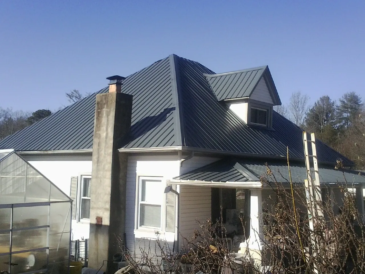 Dark blue standing seam metal roof on a white farmhouse with dormer — Slate & Tile Roof Repair by Roofing Brothers in Yoder