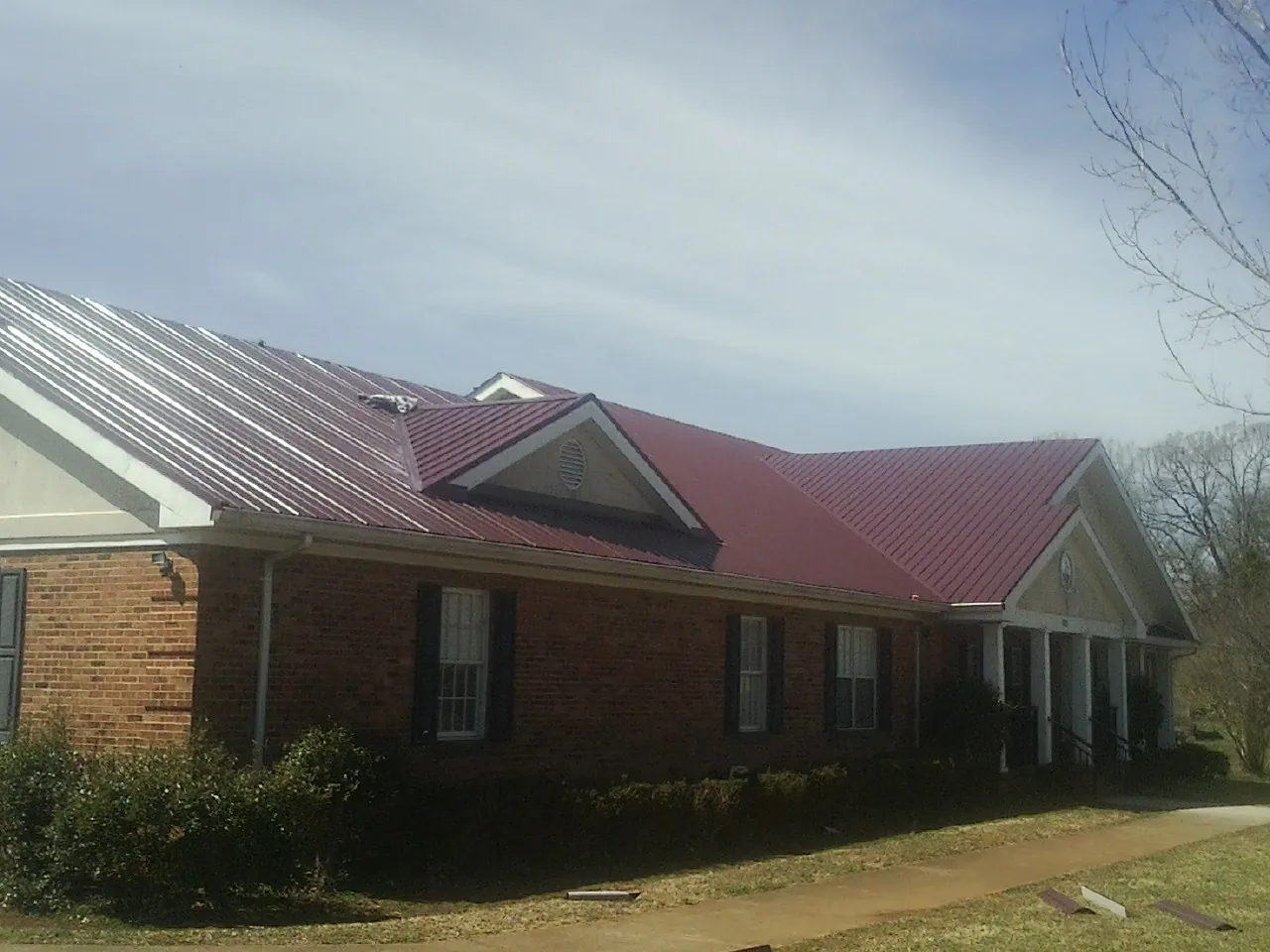 Red metal roof with gabled entries on a long brick building, from a Hail Damage Roof Repair job in Yoder