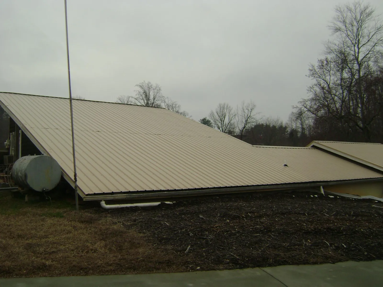 Wide tan metal roof plane seen from the ground beside a propane tank in Yoder