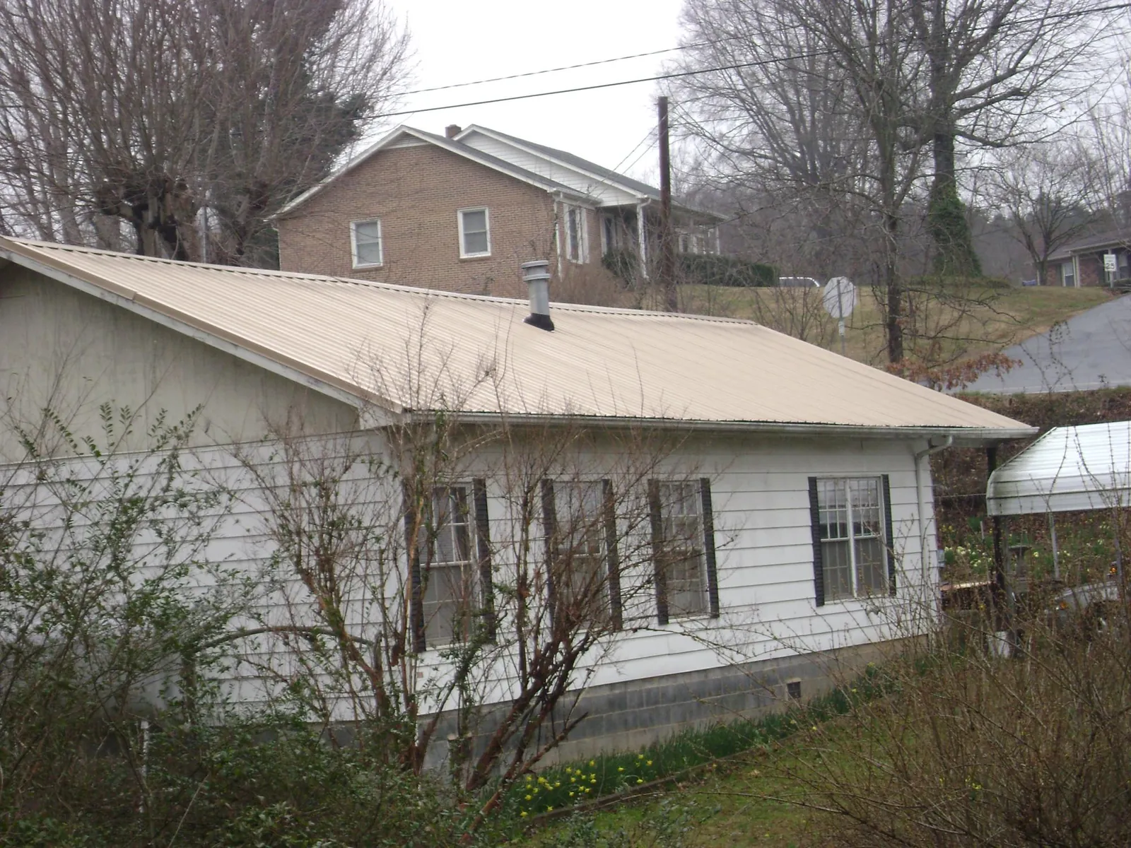 Tan metal roof on a white sided house set into a hillside — Commercial Roofing by Roofing Brothers in Yoder